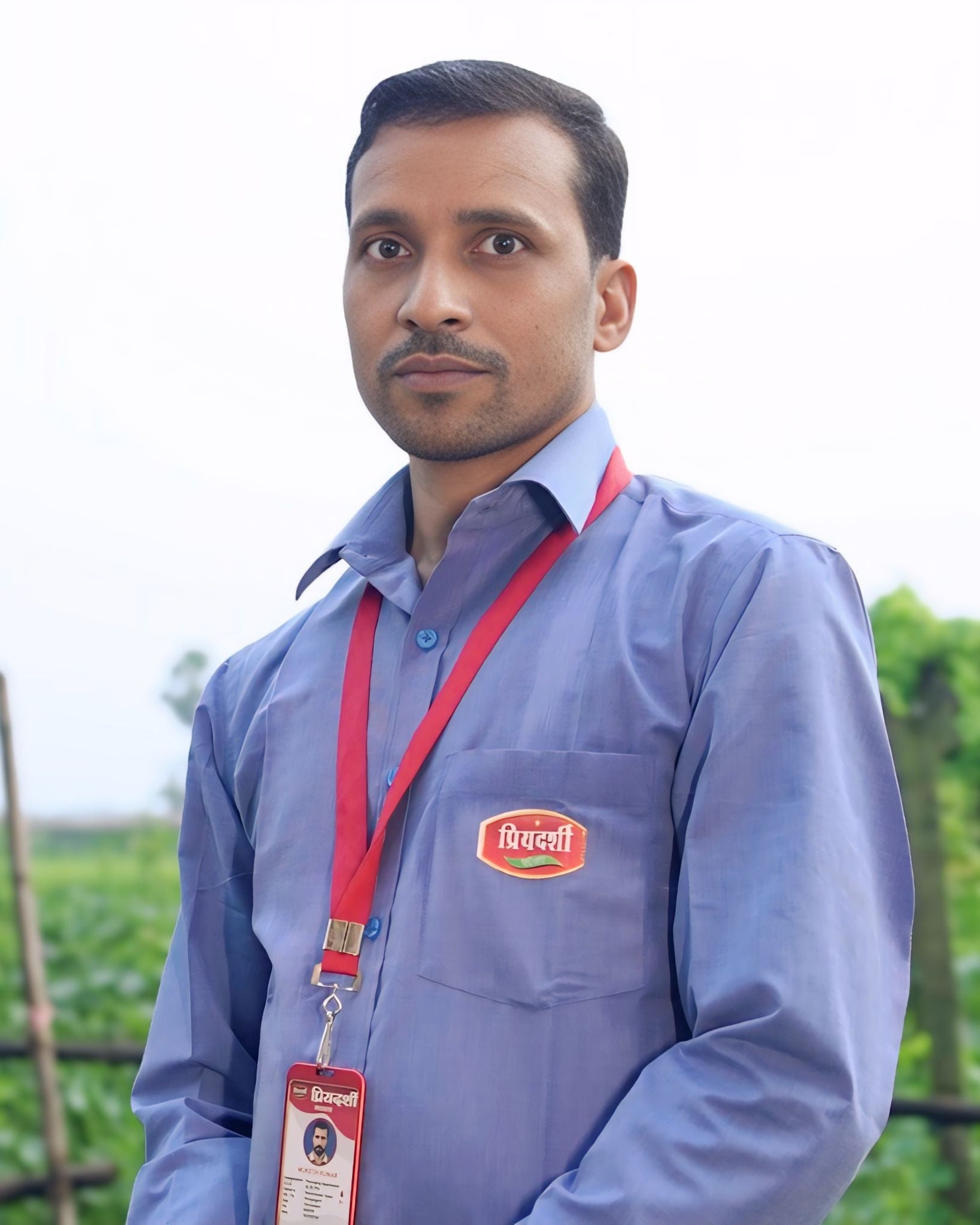 Man wearing a blue shirt with a logo and a red lanyard against a blurred outdoor background